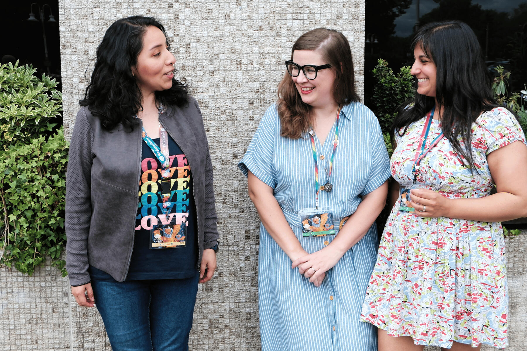Photo by Anya Good Three femme-presenting people standing talking and laughing together outdoors. Left to right, Aida, Darcy and Michelle
